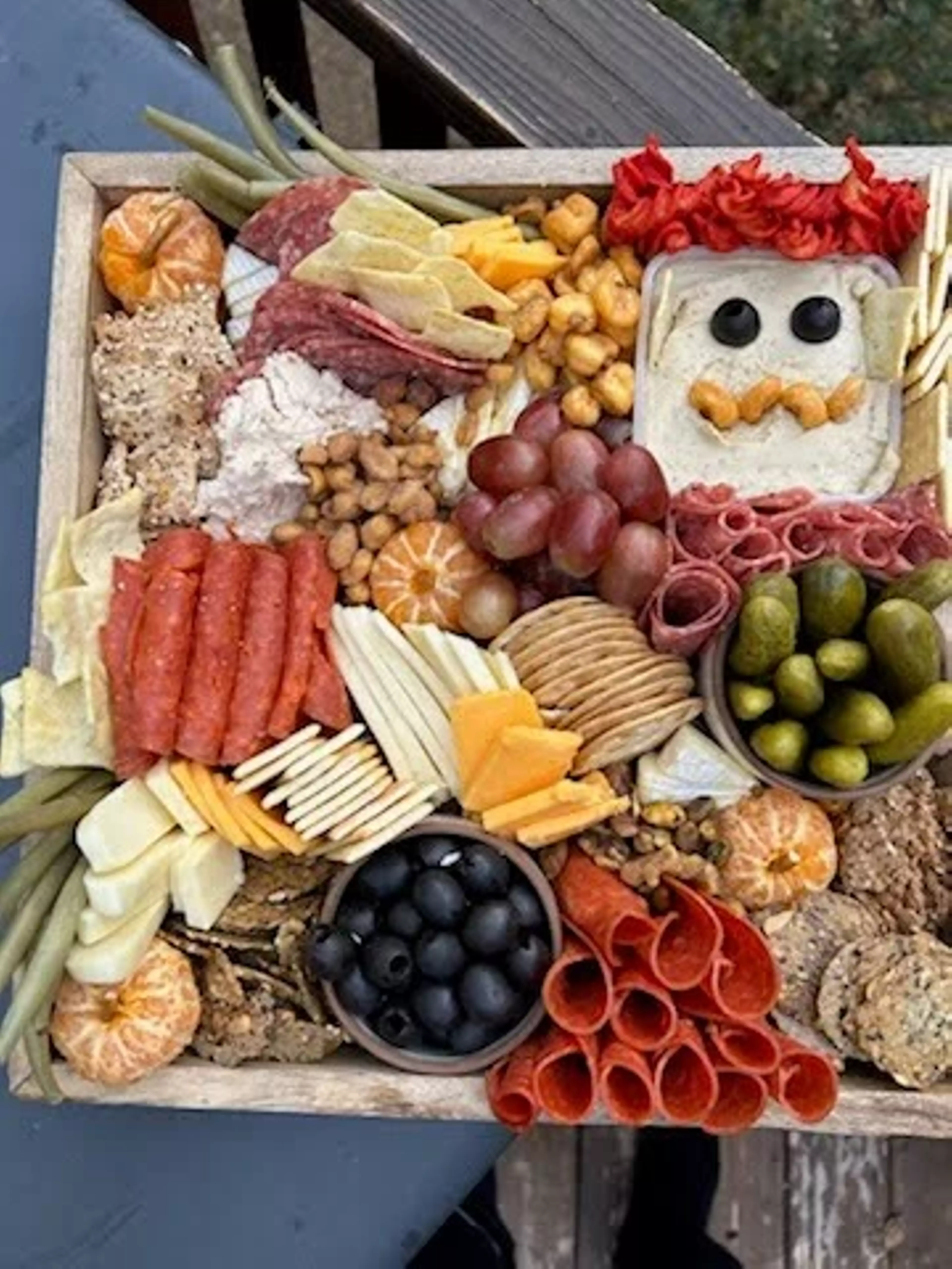 An wooden box jam-packed with gourmet smoked meats and cheeses, fruits, and crackers.