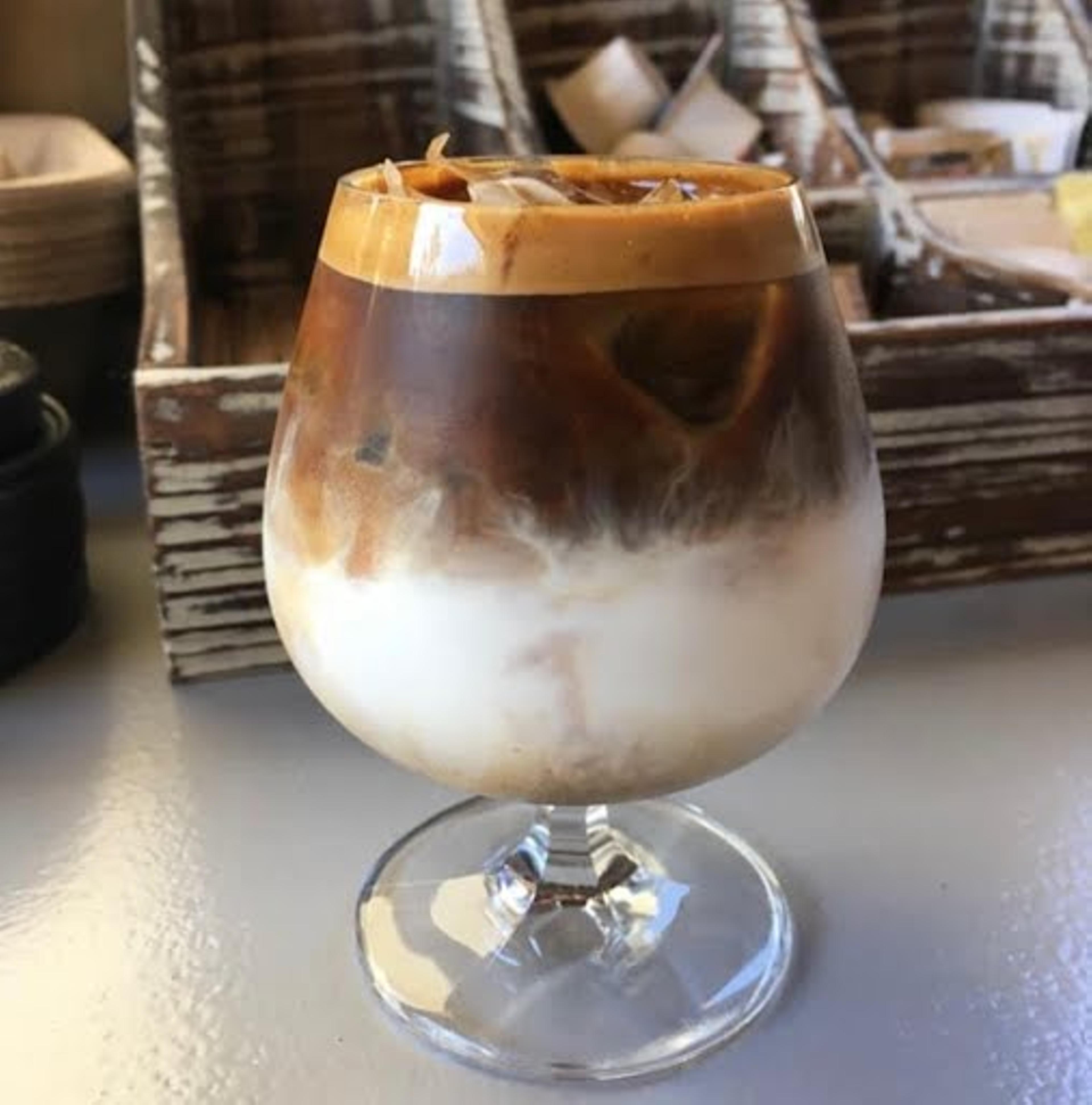 A dark-brown and white coffee drink in an elaborate round glass.